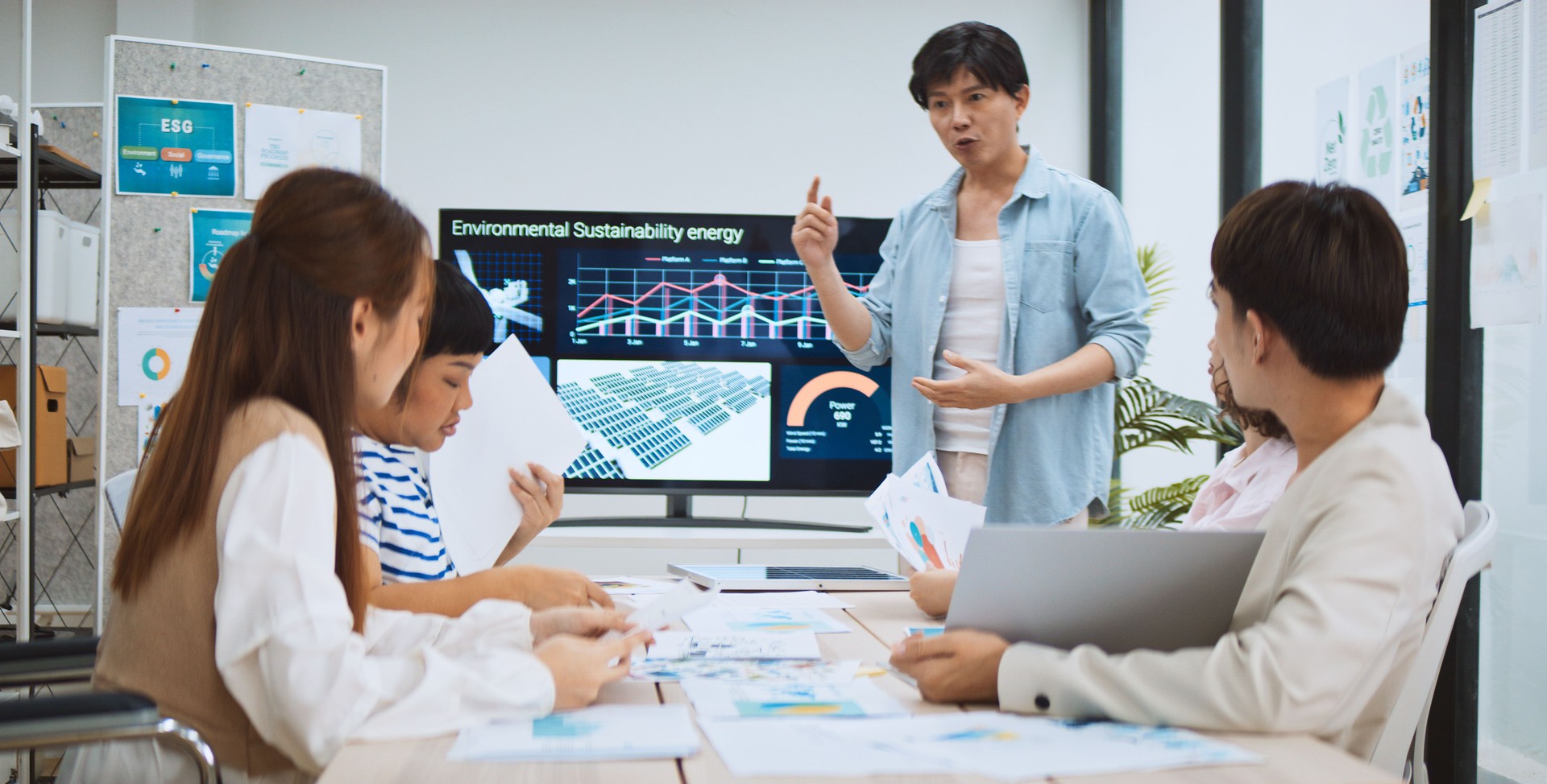 Asian business people team brainstorm meeting in sustainable corporate office. Presentation ESG project planning, solar panel, wind turbine power energy generation. Environmental conservation concept
